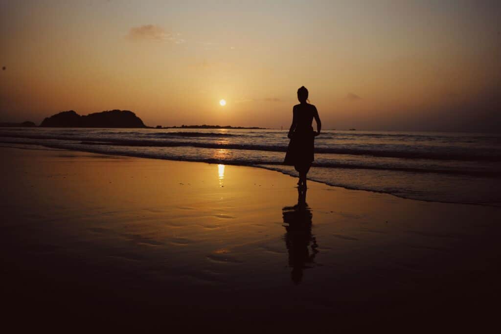 Woman standing on the beach at sunrise embracing emotional healing and forgiveness